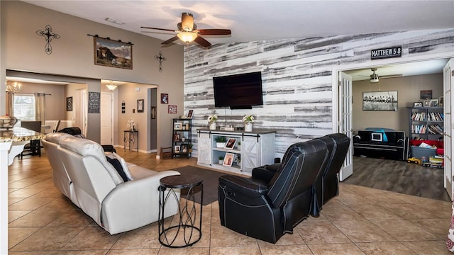 living area featuring tile patterned flooring, visible vents, ceiling fan with notable chandelier, and an accent wall