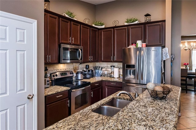 kitchen with backsplash, light stone countertops, appliances with stainless steel finishes, a notable chandelier, and a sink