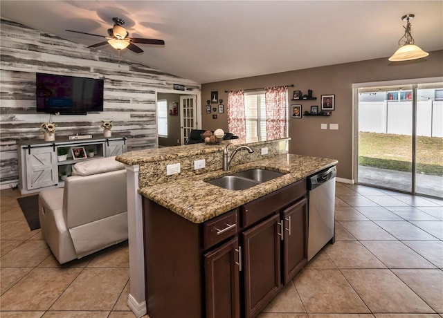 kitchen with light tile patterned floors, lofted ceiling, an island with sink, a sink, and stainless steel dishwasher