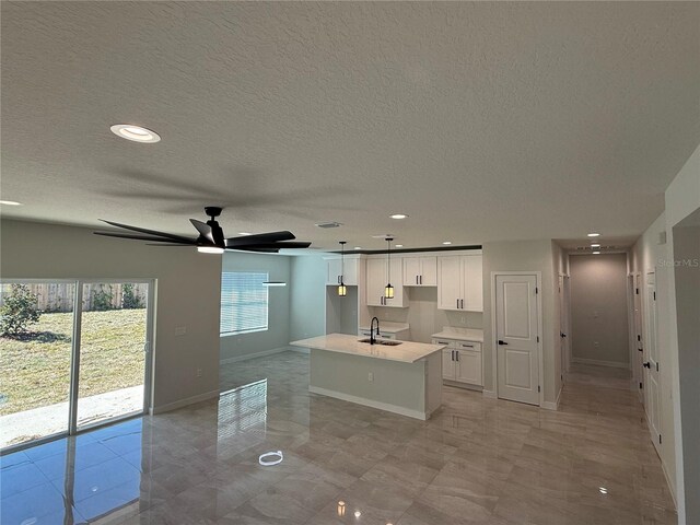 kitchen with a center island with sink, baseboards, light countertops, white cabinetry, and a sink