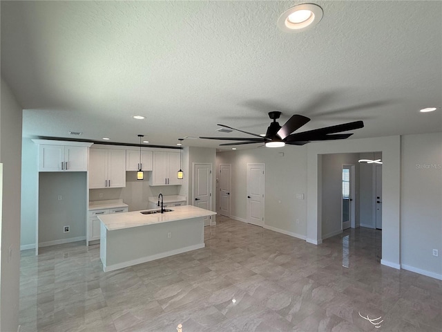 kitchen featuring light countertops, a kitchen island with sink, white cabinets, a sink, and a textured ceiling