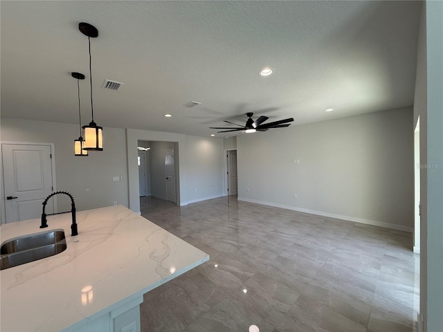 kitchen featuring visible vents, ceiling fan, light stone counters, hanging light fixtures, and a sink