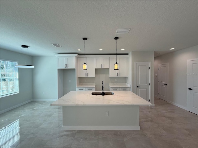 kitchen with a kitchen island with sink, a sink, visible vents, white cabinetry, and light stone countertops