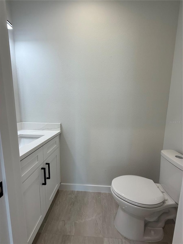 half bath with baseboards, vanity, and toilet