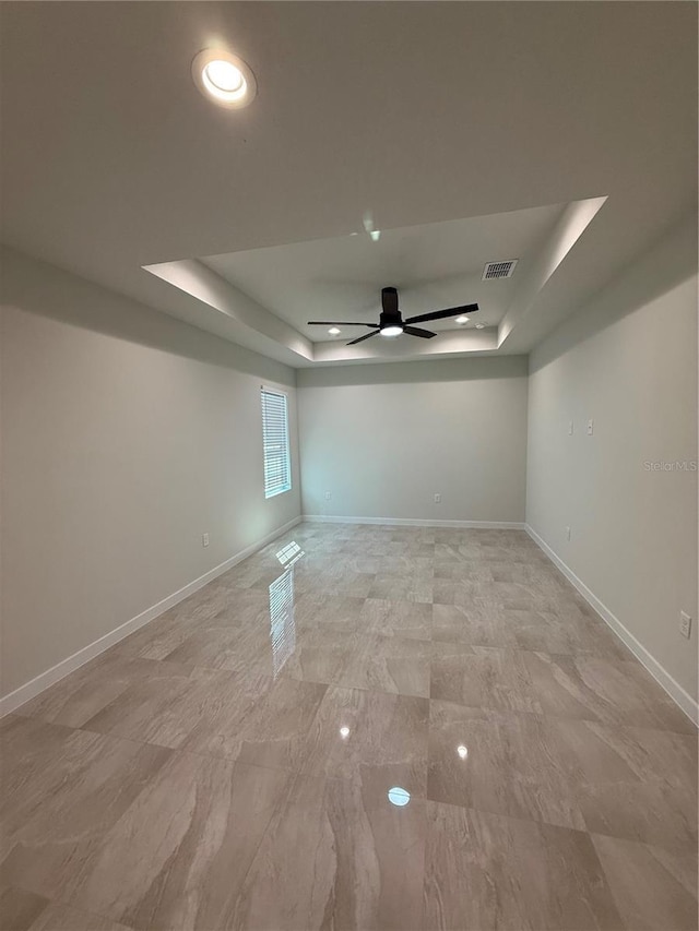 empty room with visible vents, baseboards, a raised ceiling, and a ceiling fan