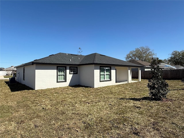 back of house featuring stucco siding, roof with shingles, fence, and a yard