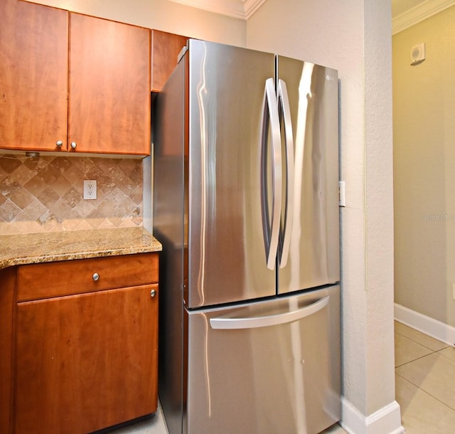 kitchen featuring baseboards, ornamental molding, light stone counters, freestanding refrigerator, and backsplash