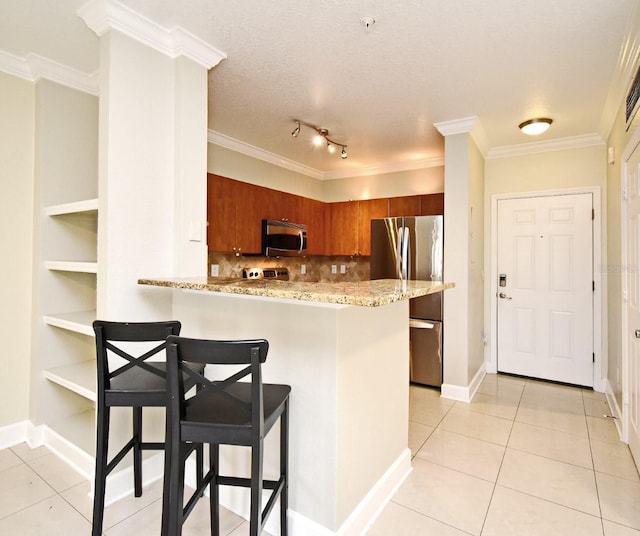 kitchen with appliances with stainless steel finishes, brown cabinetry, light tile patterned flooring, and a breakfast bar area