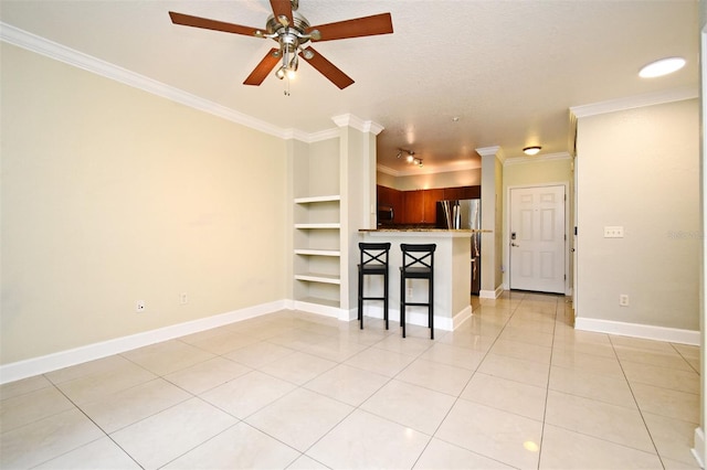 unfurnished living room with built in features, crown molding, light tile patterned floors, a ceiling fan, and baseboards