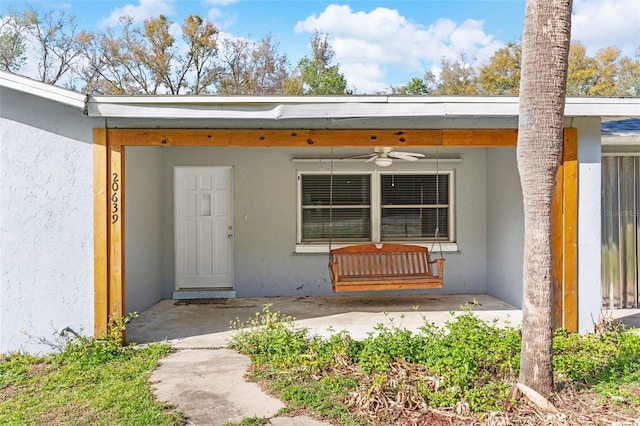 view of exterior entry with a ceiling fan and stucco siding