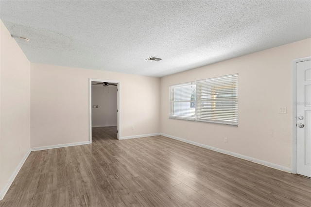spare room with a textured ceiling, wood finished floors, visible vents, and baseboards