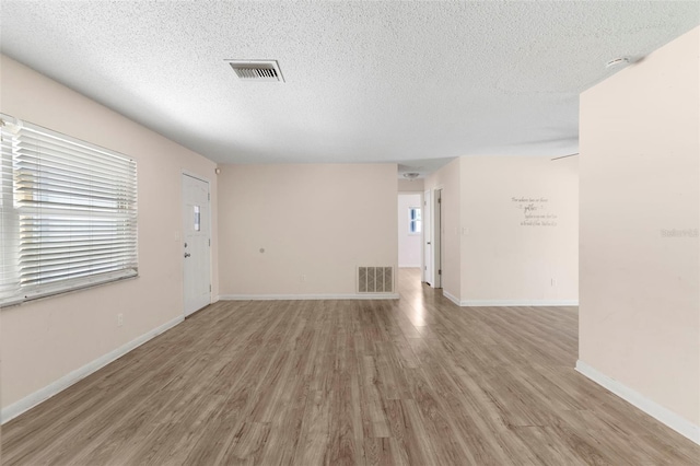 unfurnished living room featuring a textured ceiling, visible vents, and light wood-style floors