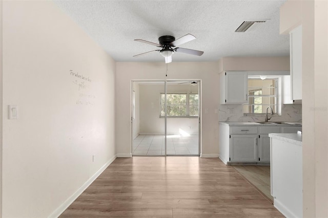 interior space with ceiling fan, a sink, visible vents, baseboards, and light wood-style floors