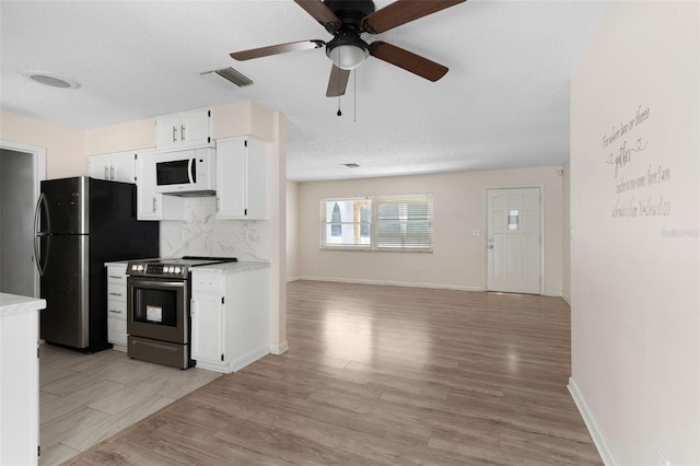 kitchen with white microwave, visible vents, freestanding refrigerator, stainless steel electric range oven, and tasteful backsplash