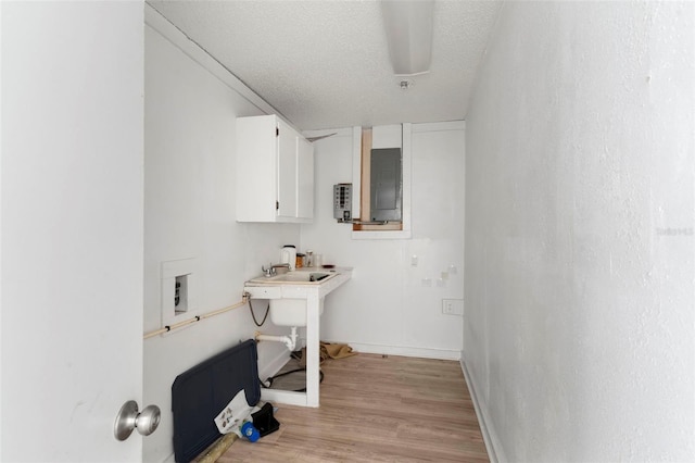 laundry area with a textured ceiling, baseboards, electric panel, and light wood-style floors