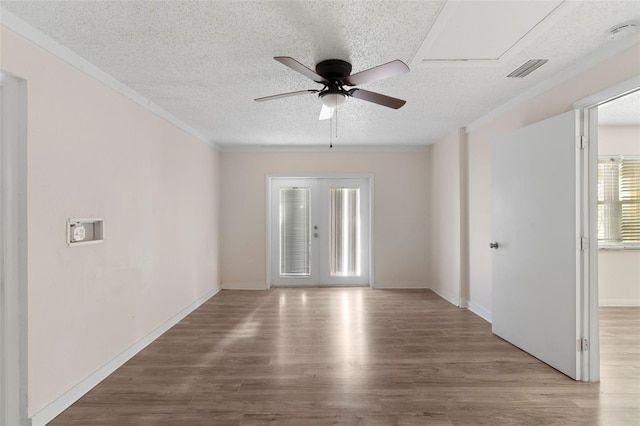 spare room with a textured ceiling, wood finished floors, visible vents, ornamental molding, and french doors