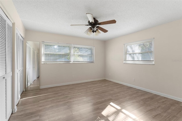 unfurnished bedroom with multiple windows, light wood-style flooring, and baseboards