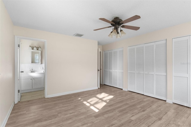 unfurnished bedroom featuring baseboards, visible vents, ensuite bath, light wood-type flooring, and two closets