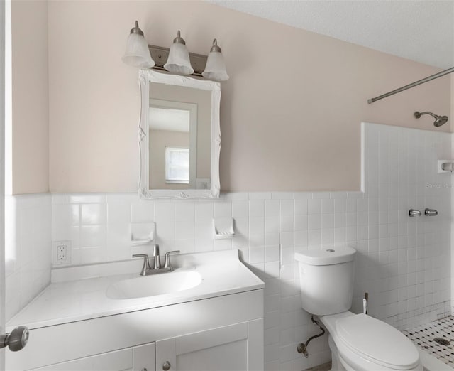 bathroom with toilet, vanity, tile walls, wainscoting, and a tile shower