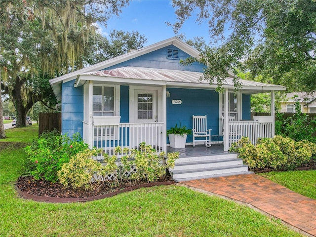 bungalow-style home featuring covered porch, metal roof, and a front yard