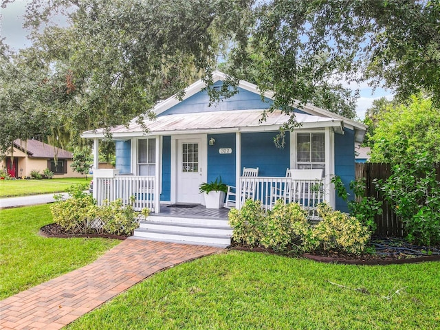 bungalow-style house with a front yard, fence, covered porch, and metal roof