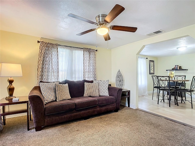 carpeted living area with baseboards, visible vents, arched walkways, a ceiling fan, and a textured ceiling