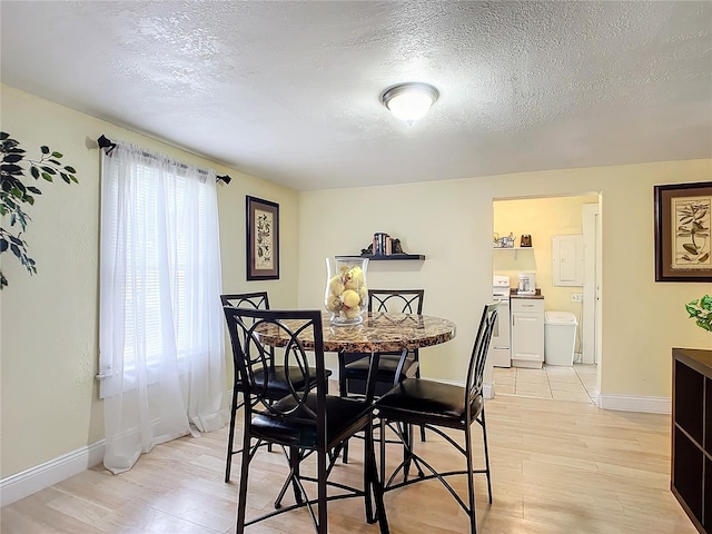 dining space with light wood-type flooring, a textured ceiling, and baseboards