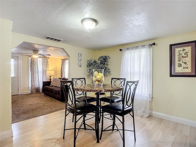 dining room featuring arched walkways, visible vents, plenty of natural light, and light wood finished floors