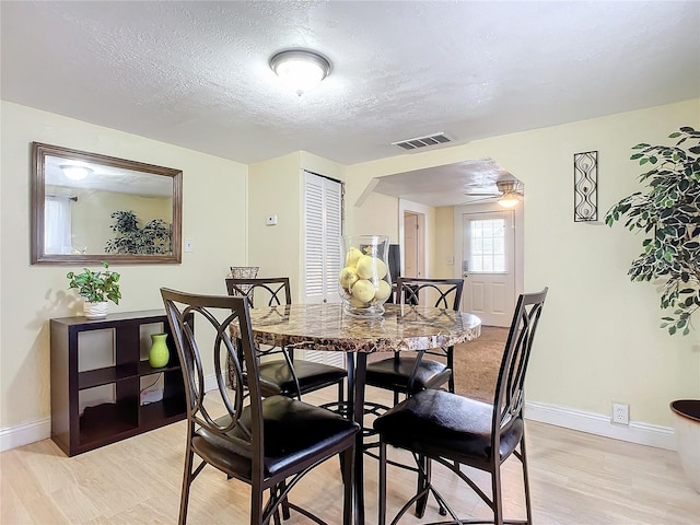 dining area with baseboards, visible vents, light wood-style flooring, and a textured ceiling