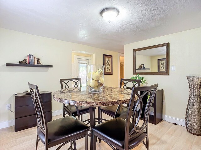 dining space featuring a textured ceiling, light wood-type flooring, and baseboards