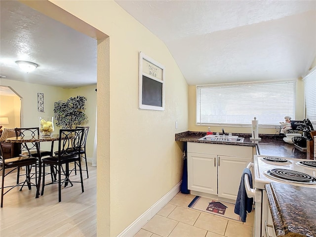 kitchen with baseboards, range with electric cooktop, a textured ceiling, white cabinetry, and a sink