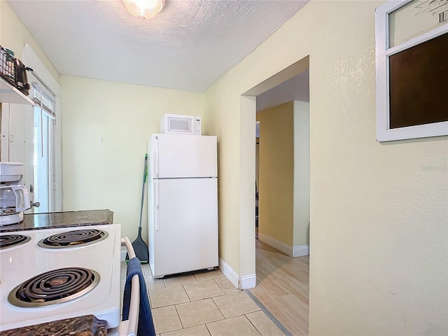 kitchen with white appliances, baseboards, a textured ceiling, and light tile patterned flooring