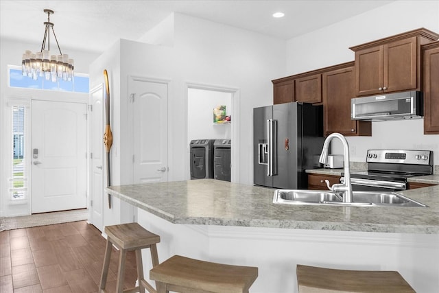 kitchen with washing machine and dryer, stainless steel appliances, light countertops, a kitchen bar, and pendant lighting