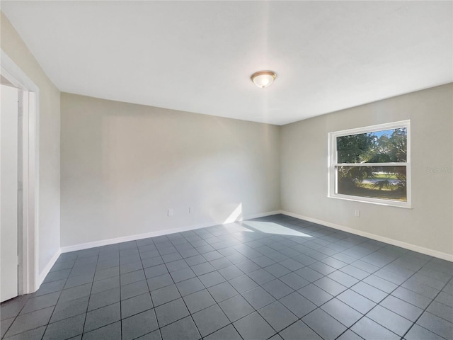 unfurnished room with dark tile patterned floors and baseboards