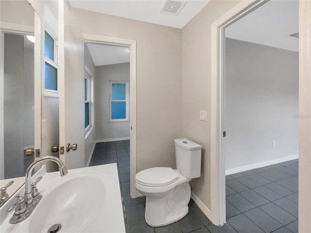 bathroom featuring baseboards, visible vents, toilet, tile patterned floors, and a sink