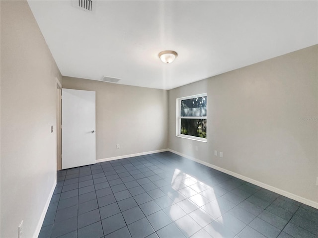 unfurnished room with dark tile patterned flooring, visible vents, and baseboards