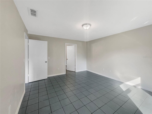 spare room with dark tile patterned floors, baseboards, and visible vents