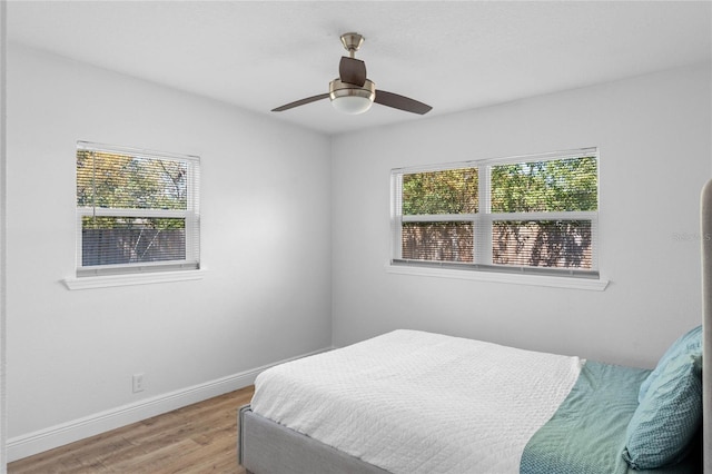 bedroom with multiple windows, wood finished floors, a ceiling fan, and baseboards