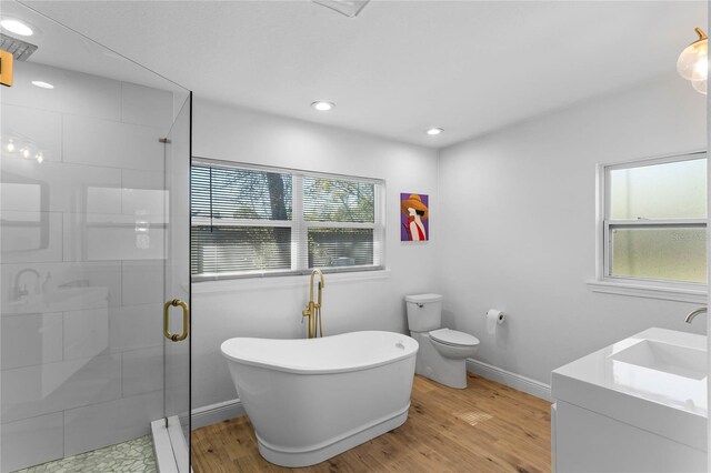 full bath featuring a freestanding tub, toilet, wood finished floors, baseboards, and a stall shower