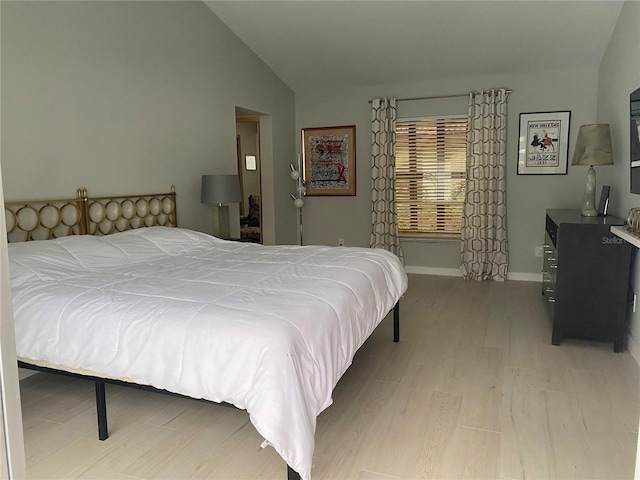 bedroom featuring lofted ceiling, baseboards, and light wood-style floors