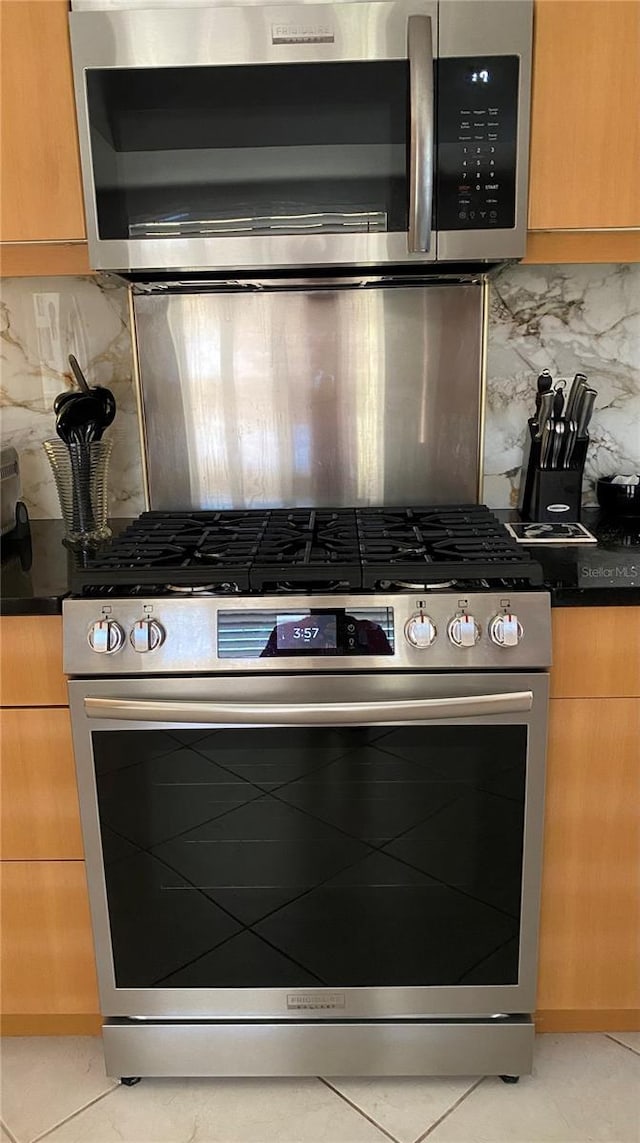 kitchen with appliances with stainless steel finishes, dark countertops, light tile patterned floors, and tasteful backsplash