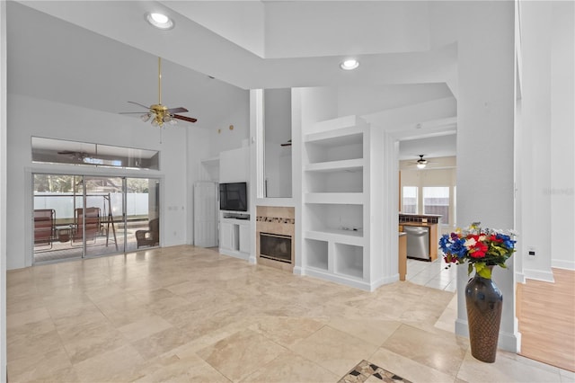 living area featuring high vaulted ceiling, ceiling fan, built in features, and a tile fireplace