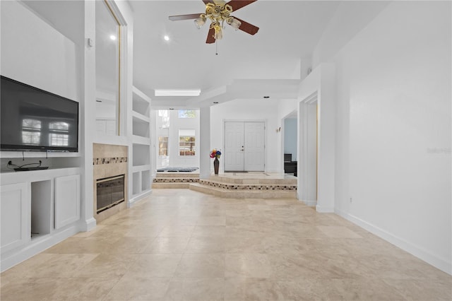 unfurnished living room featuring built in features, a tile fireplace, baseboards, and a ceiling fan