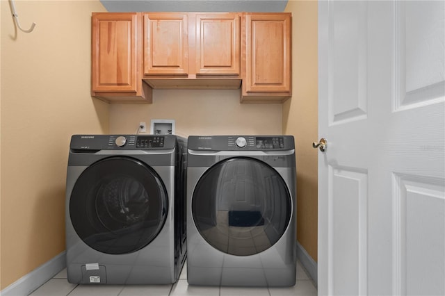 washroom featuring cabinet space, washing machine and dryer, baseboards, and light tile patterned flooring