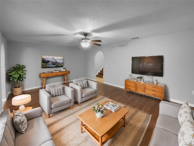 living area with arched walkways, visible vents, a textured ceiling, wood finished floors, and baseboards