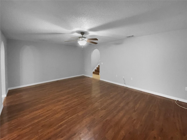 spare room with arched walkways, visible vents, dark wood-type flooring, a textured ceiling, and baseboards