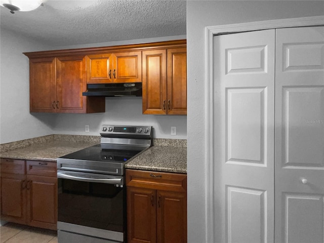 kitchen featuring brown cabinetry, stainless steel electric stove, a textured ceiling, under cabinet range hood, and light tile patterned flooring