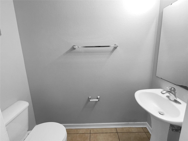 half bath with toilet, baseboards, a sink, and tile patterned floors