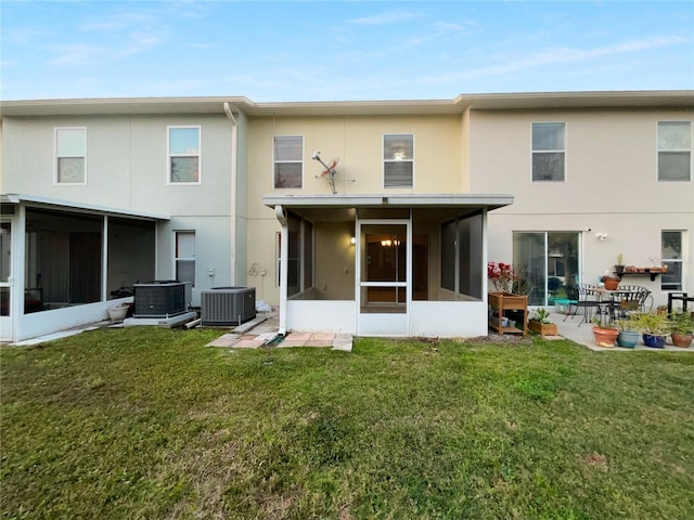 rear view of property with a sunroom, stucco siding, a lawn, and central AC unit