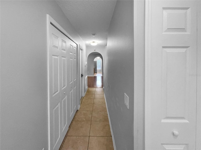 corridor with arched walkways, a textured ceiling, baseboards, and light tile patterned floors